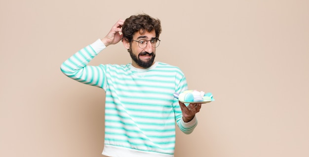 Young man with macaroons against flat wall