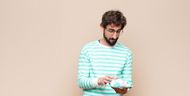 Young man with macaroons against flat wall