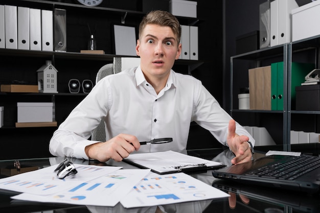 Young man with magnifying glass and insurance is sitting at table in bright office