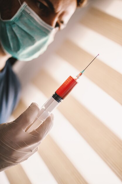 Young man with mask and gloves looking at injection full with
blood. be responsible, stay at home. world pandemic.