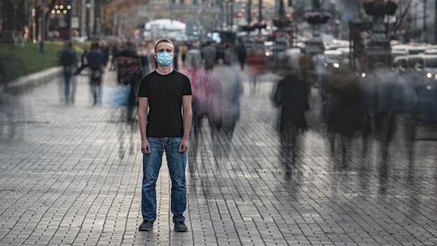 The young man with medical face mask stands on the crowded street