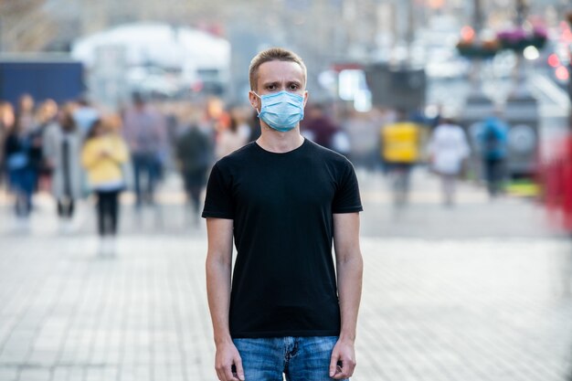 The young man with medical mask on his face stands on the urban street