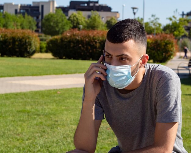 A young man with a medical mask in the park speaks on the mobile phone