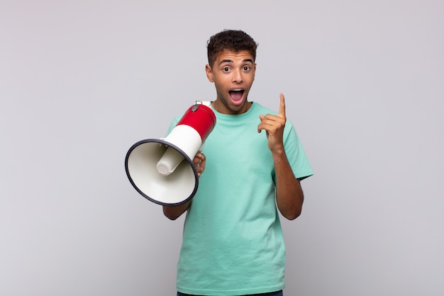 Young man with a megaphone feeling like a happy and excited genius after realizing an idea, cheerfully raising finger, eureka!