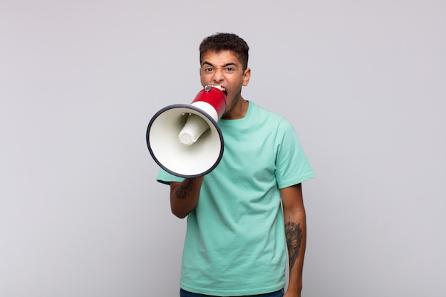 Young man with a megaphone shouting aggressively, looking very angry, frustrated, outraged or annoyed, screaming no