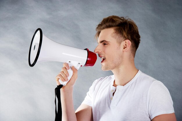 Photo young man with megaphone standing against gray backdrop