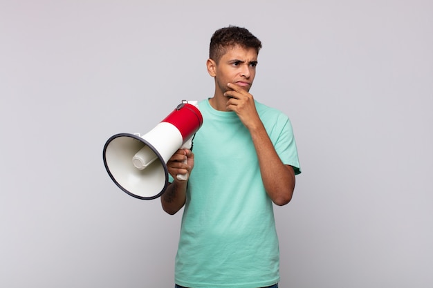 young man with a megaphone thinking, feeling doubtful and confused, with different options, wondering which decision to make