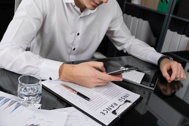 Young man with mobile phone in his hands sitting at table in bright office