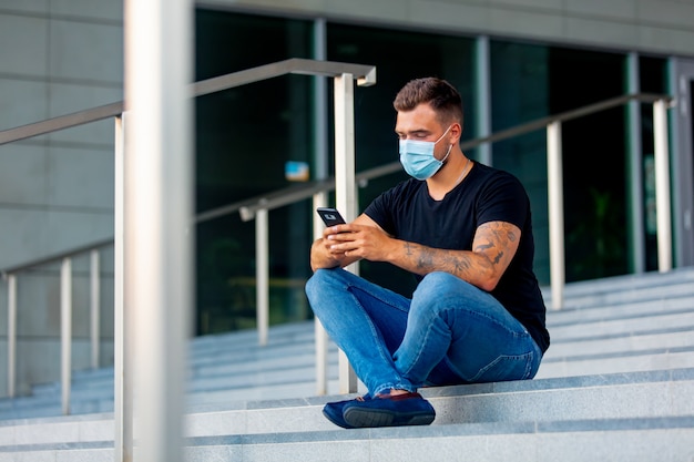 Young man with mobile phone on the steps of the University campus