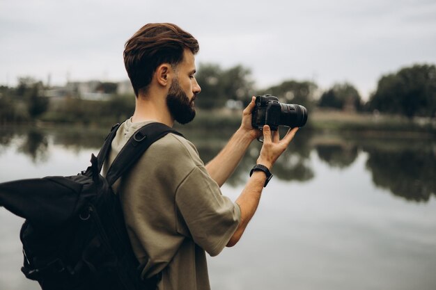 Молодой человек с современной зеркальной камерой в руках на естественном фоне