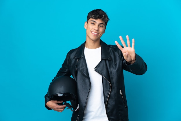 Young man with a motorcycle helmet over blue happy and counting four with fingers