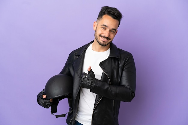 Young man with a motorcycle helmet isolated on purple background giving a thumbs up gesture