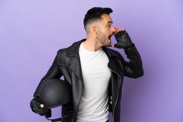 Giovane con un casco da motociclista isolato su sfondo viola che grida con la bocca spalancata di lato