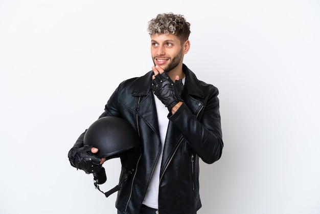 笑顔で見上げる白い背景で隔離のオートバイのヘルメットを持つ若い男