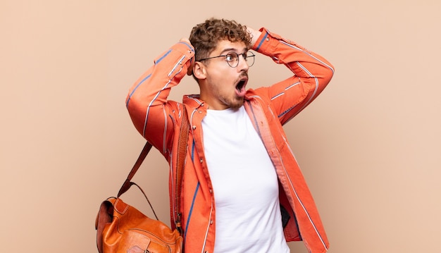 Young man with open mouth, looking horrified and shocked because of a terrible mistake, raising hands to head