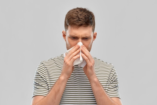 young man with paper tissue blowing his nose