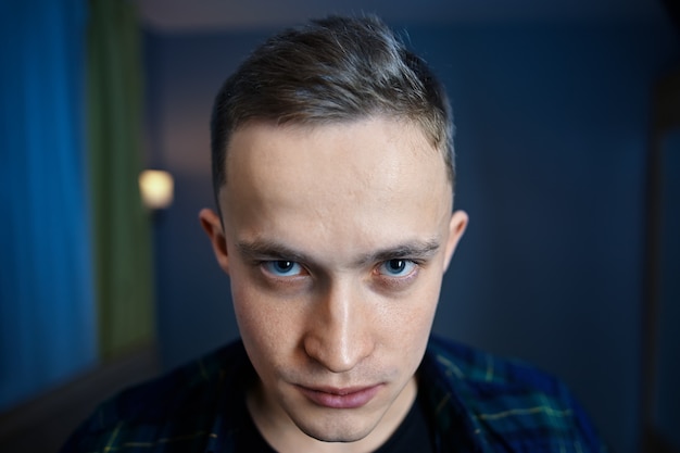 Young man with paranoid schizophrenia looks out from under his eyebrows with hatred.