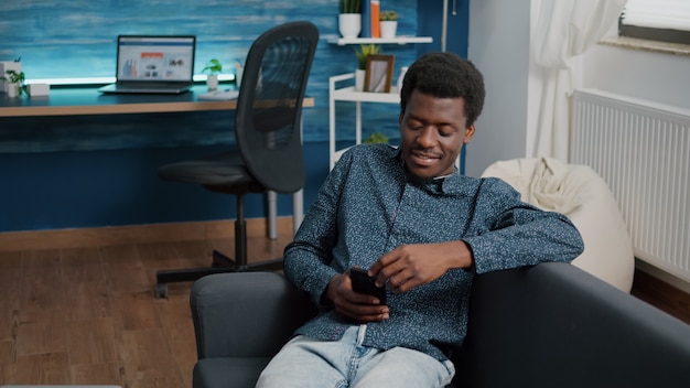 young man with phone in hands looking at online streaming services content, enjoying working from home