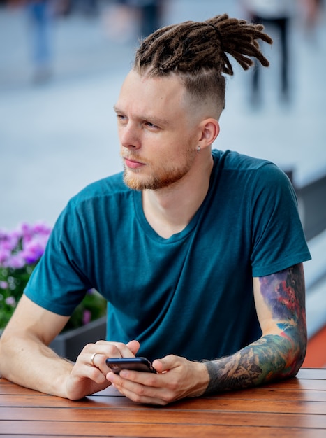 Young man with phone is sitting at table in a cafe in the city