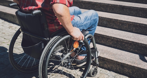 Young man with a physical disability who uses wheelchair in\
front of the stairs