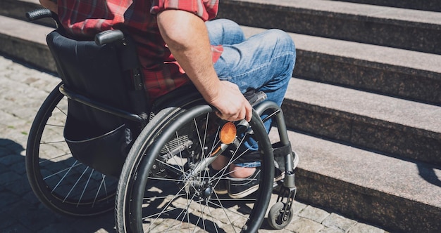 Young man with a physical disability who uses wheelchair in front of the stairs