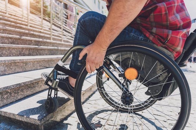 Молодой человек с ограниченными физическими возможностями, который использует инвалидную коляску перед лестницей