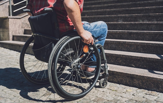 Young man with a physical disability who uses wheelchair in\
front of the stairs