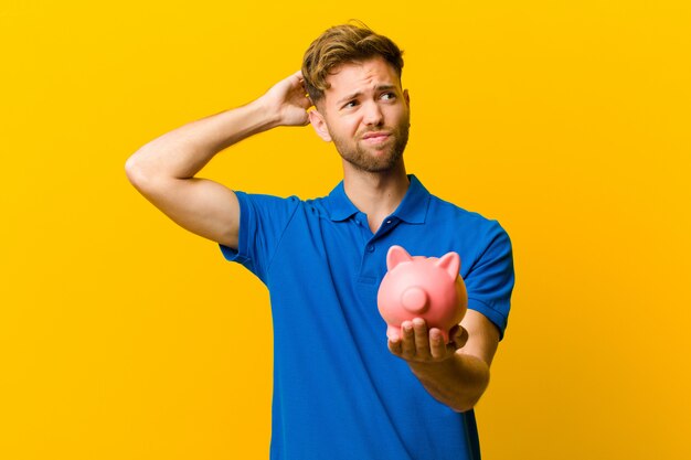 Young man with a piggy bank against orange background