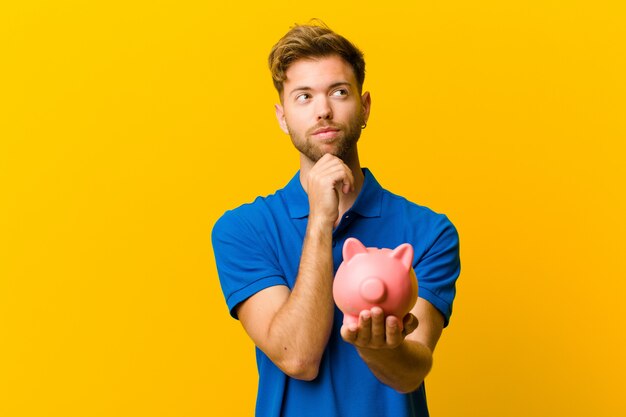 Young man with a piggy bank against orange background