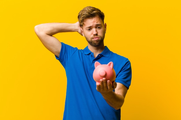 Young man with a piggy bank against orange background