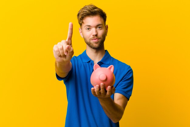 Young man with a piggy bank against orange wall