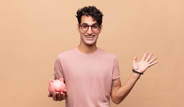 Young man with a piggy bank feeling happy, surprised and cheerful, smiling with positive attitude, realizing a solution or idea