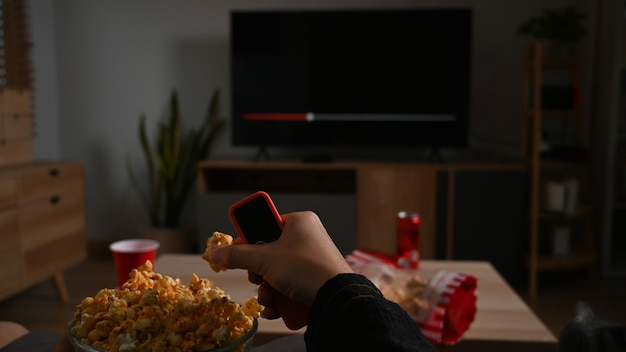 Молодой человек с попкорном и пультом дистанционного управления во время просмотра фильма в своей гостиной ночью
