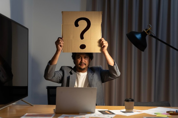 Young man with a question sign on a card covering face Employees dilemma with question mark on blank paper Confused Thinking Brainstorming or Decision