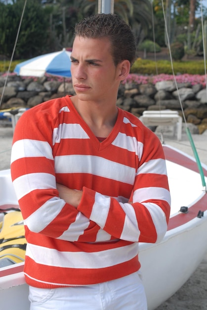 Young man with sailor look in a coastal area between sailboats