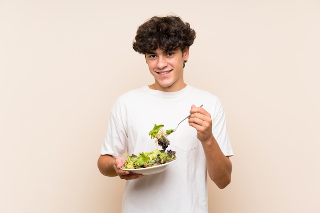 Young man with salad over isolated green wall