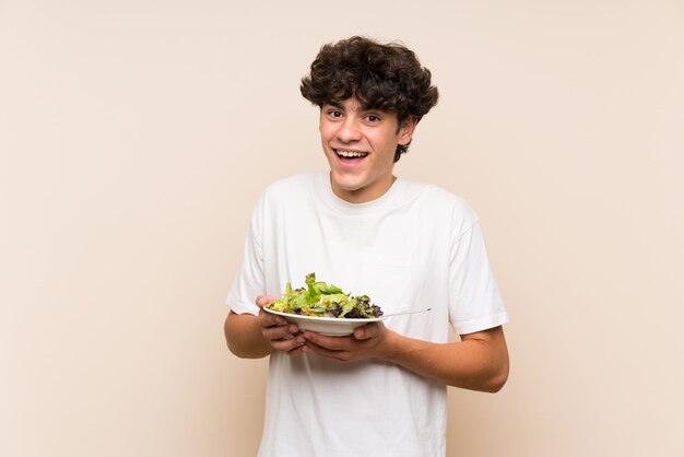 Young man with salad over isolated green wall