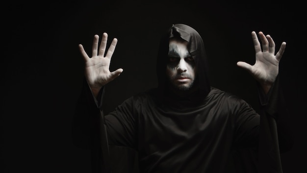 Фото Молодой человек со страшным макияжем, одетый как мрачный жнец на хэллоуин.