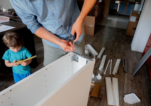 Young man with screwdriver and a child are instaling a furniture 