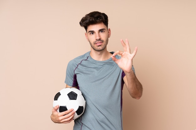 Молодой человек с футбольным мячом и делая знак ОК
