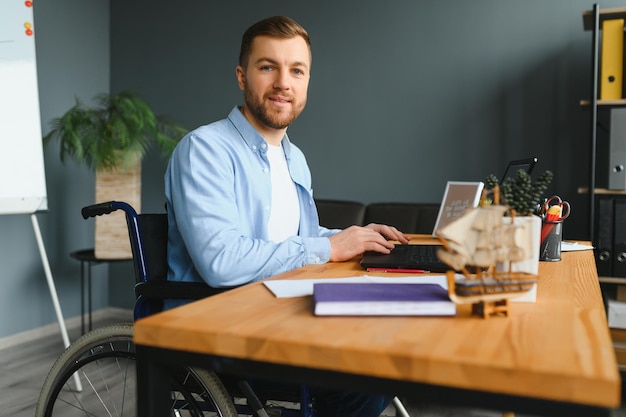 Young man with special needs in casual clothes working on wireless laptop Male freelancer working from home while sitting in wheelchair