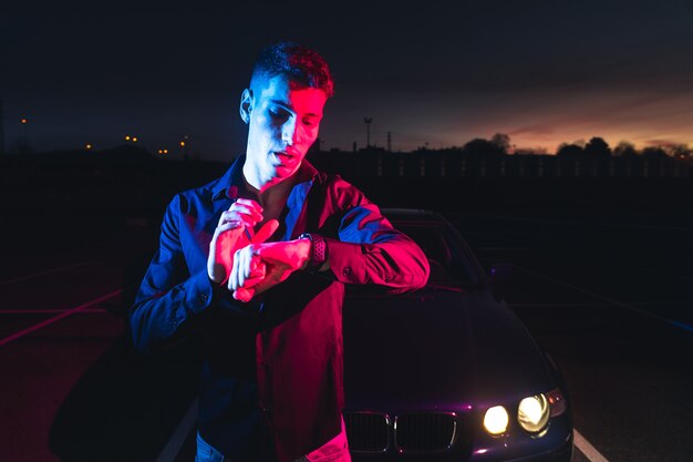 Young man with a sports car at a parking lot with color lights