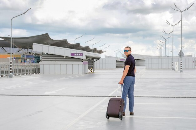 Young man with a suitcase in his hands in an empty parking lot outdoors