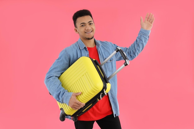 Young man with suitcase on pink background