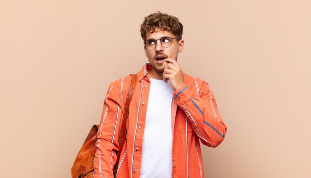 Young man with surprised, nervous, worried or frightened look, looking to the side towards copy space