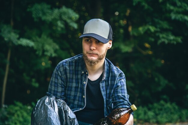 A young man with a trash bag in the forest cleans up plastic
bottles