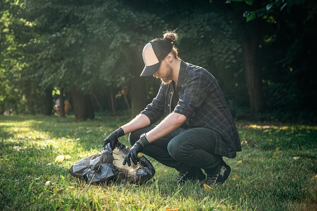 A young man with a trash bag in the forest cleans up plastic bottles