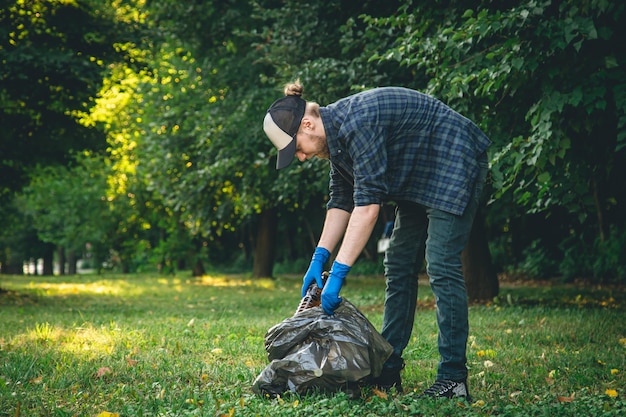 A young man with a trash bag in the forest cleans up plastic bottles