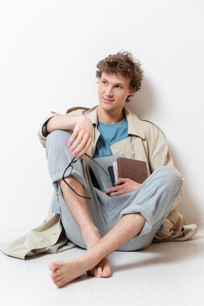 Foto giovane uomo con trench con gli occhiali e tenendo i libri