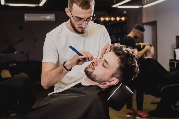 Giovane con taglio di capelli alla moda al negozio di barbiere. il barbiere fa taglio di capelli e barba.